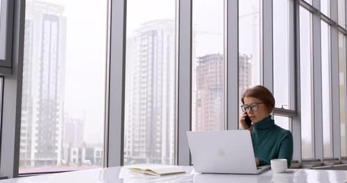 Young business woman talking on the phone while working on laptop at workplace in office