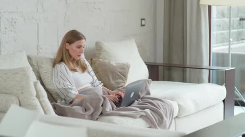 Une femme est assise sur le canapé à la maison et travaille à l'aide d'un gestionnaire d'ordinateur portable sur un travail à distance pendant