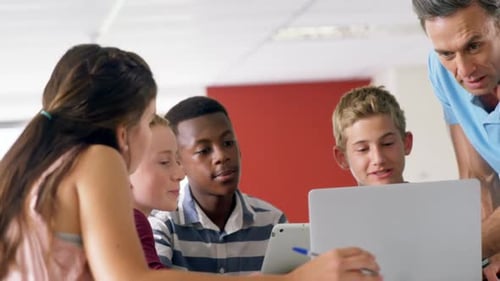 Teacher assisting schoolkids on laptop