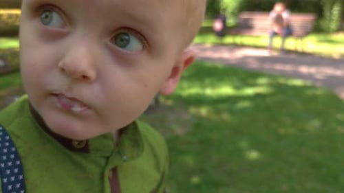 Fair-Haired Child Eats Outdoors In a Sunny Park