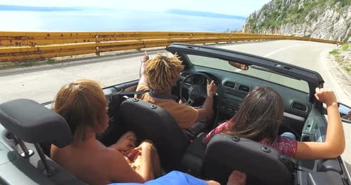 Amigos divirtiéndose conduciendo por la carretera a lo largo de la costa en un convertible rojo