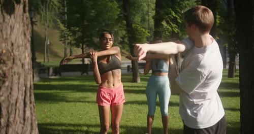 Guy Trainer Shows Exercise and Women Do Warmup Among Trees