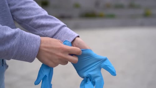 Person Putting on Blue Protective Gloves in Urban Setting
