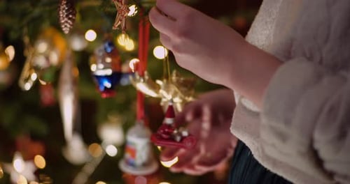 Person Decorates Christmas Tree with Colorful Ornaments