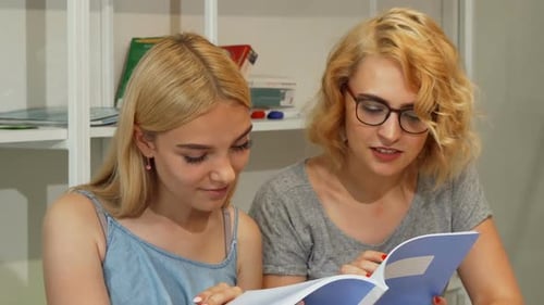 Young Female Students Reading Textbook at College Auditorium