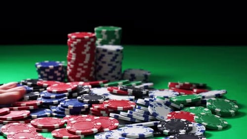 Hand Counts Poker Chips Lying on a Green Table on a Black Background in Close-up