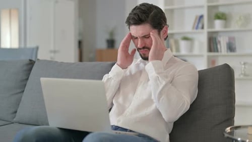 Man on Couch With Headache Uses Laptop