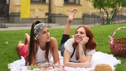 Two Women Having Picnic Together Laying on the Plaid on the Park Lawn in Summer