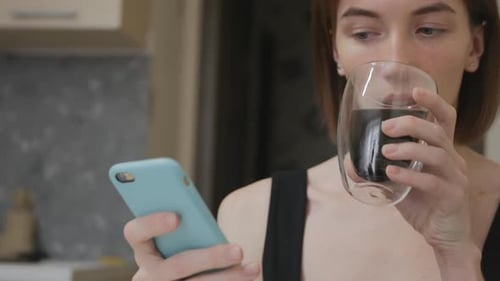 Woman Drinks and Uses Cellphone Indoors