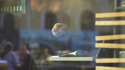 Atractiva estudiante en ropa árabe tradicional libro de lectura en café