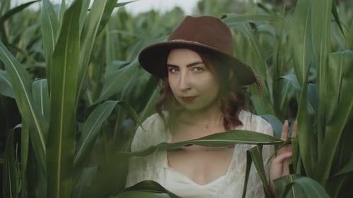 Portrait of Beautiful Young Girl in Hat Standing at a Corn Field Smiling and Looking at Camera in