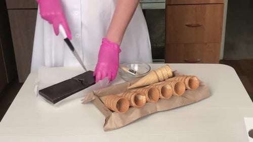 A Woman Cracks A Bar Of Chocolate. Next To The Waffle Cones.