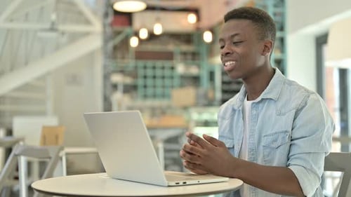 African Man Doing Video Chat on Laptop in Cafe