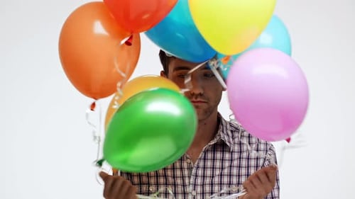 Man in Birthday Hat Holds Balloons Looks Depressed