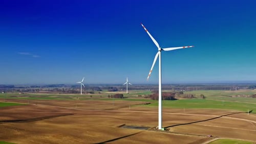 White wind turbine on brown field with blue sky, aerial view