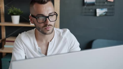 Slow Motion Portrait of Serious Young Man in Glasses Looking at Monitor Working in Office