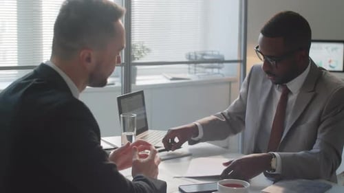 Two Multiethnic Businessmen Signing Contract and Shaking Hands in Office
