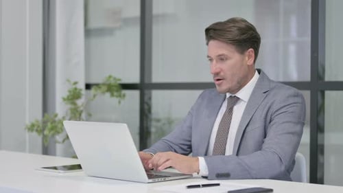 Middle Aged Man Celebrating while using Laptop in Office on Bench