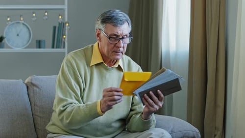 Mature Man Sorting Mail on Couch Indoors