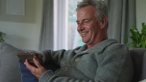 Laughing Man Relaxing on Couch with Tablet Indoors