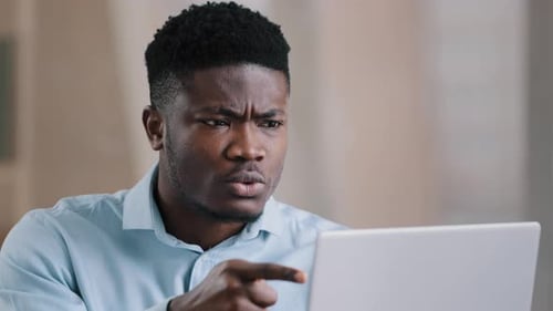 Man Points Frustrated at Laptop Screen Indoors