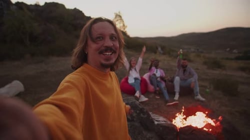 Man Makes Video of Himself and His Friends Sitting Around Campfire in Nature on the Front Camera