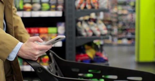 Close Up of Man Hand Holding Smartphone and Srolling Screen in Supermarket