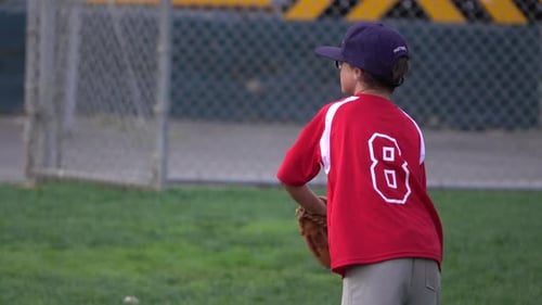 A boy practices playing catch on a little league baseball field.