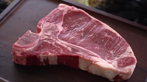 Raw Bone-In Steak on Dark Wooden Surface