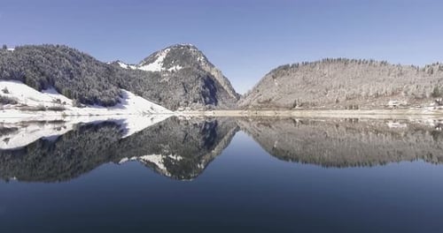 Die
Movind-Drohne schoss über einen spiegelnden See in den Schweizer Bergen. Mit Schnee bedeckter Berg.