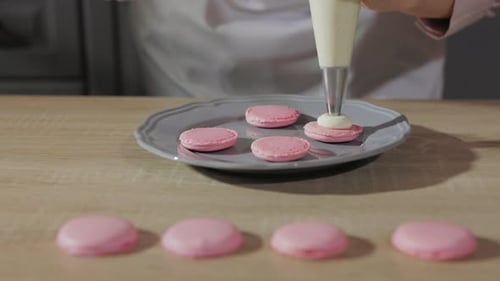 Pastry Chef Piping Out Chocolate Cream on Pink Macarons Shells, Close Up, Details