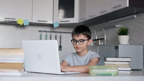 Kind, ein Schüler mit Brille, unterrichtet zu Hause Unterricht und sitzt in der Küche am Tisch