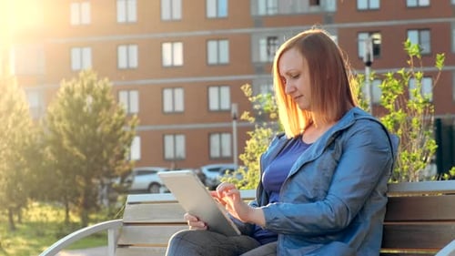 Woman Using Tablet Computer Sitting on Bench in City