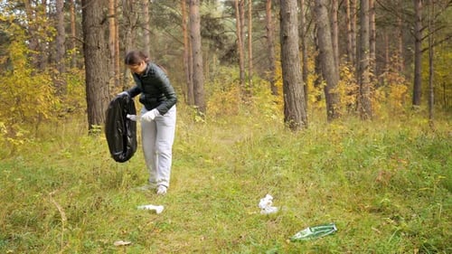 Mujer joven recoge basura en un paquete negro en el bosque