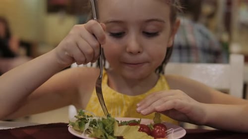 Little Girl Eat Green Salad with Appetite in the Restaurant. Good Health Concept