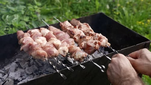 Cocinando carne en brasas, el hombre gira brochetas, primer plano de sus manos, cocina en la naturaleza