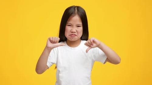 Displeased Girl Giving Thumbs Down on Yellow Background