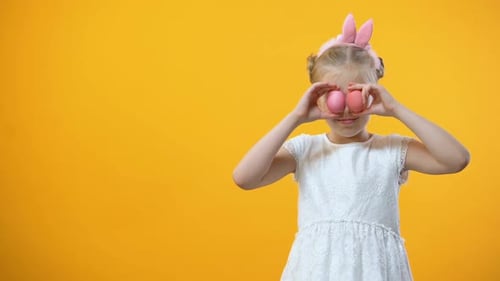 Happy Little Girl Holding Colored Easter Eggs in Front Eyes and Smiling Camera