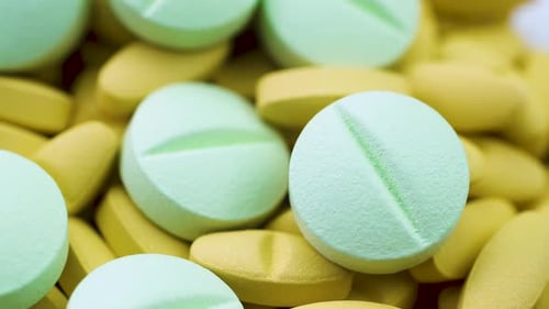 Large Round Green Pills Lie on Bright Yellow Antibiotics. Close Up Rotation