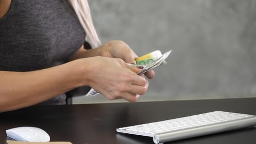 Woman Counting Euro Banknotes at Computer Desk