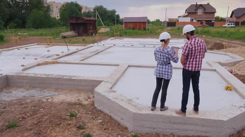 Two Buildersa Man and a Woman are on the Foundation of the Future Building Discussing the Work Plan