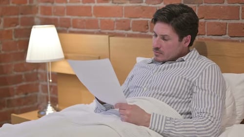 Man Reading Documents in Bedroom