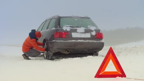 Man Changes Tire on Car in Snowy Rural Setting