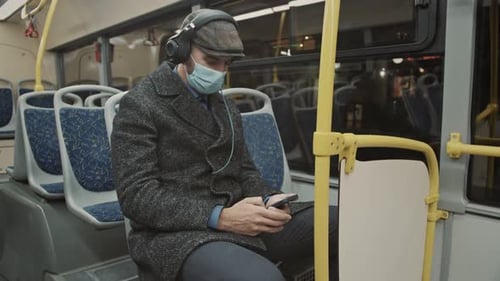 Man Wearing Mask Using Phone on Bus at Night