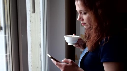 Woman Drinking Tea and Using Smartphone Indoors