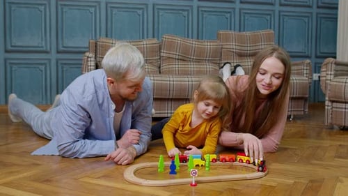 Young Mother and Father Playing with Child Daughter Riding Toy Train on Wooden Railroad Game at Home
