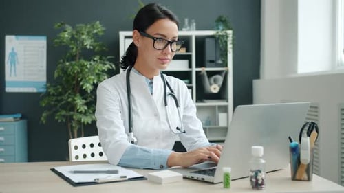 Portrait of Young Female Doctor in Uniform Working with Laptop Computer in Office