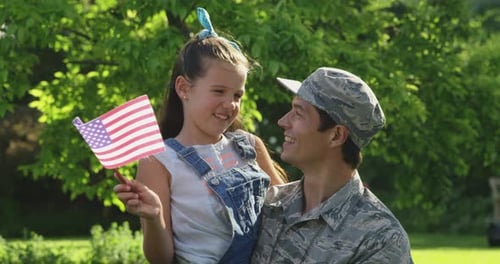 Man in Uniform Holds Child With American Flag