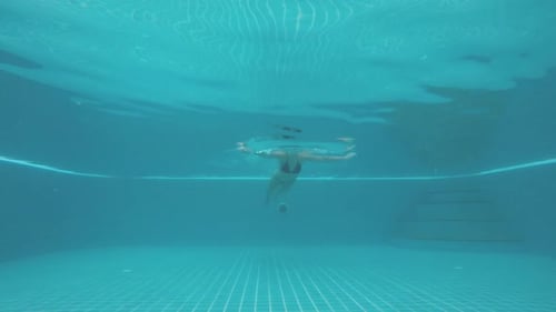 Toma submarina del cuerpo de una mujer nadando hacia la cámara en la piscina