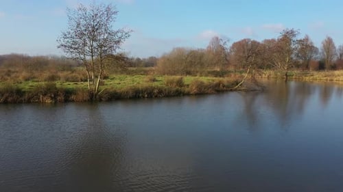 Flying over a large river following the riverbanks with small trees and broad fields